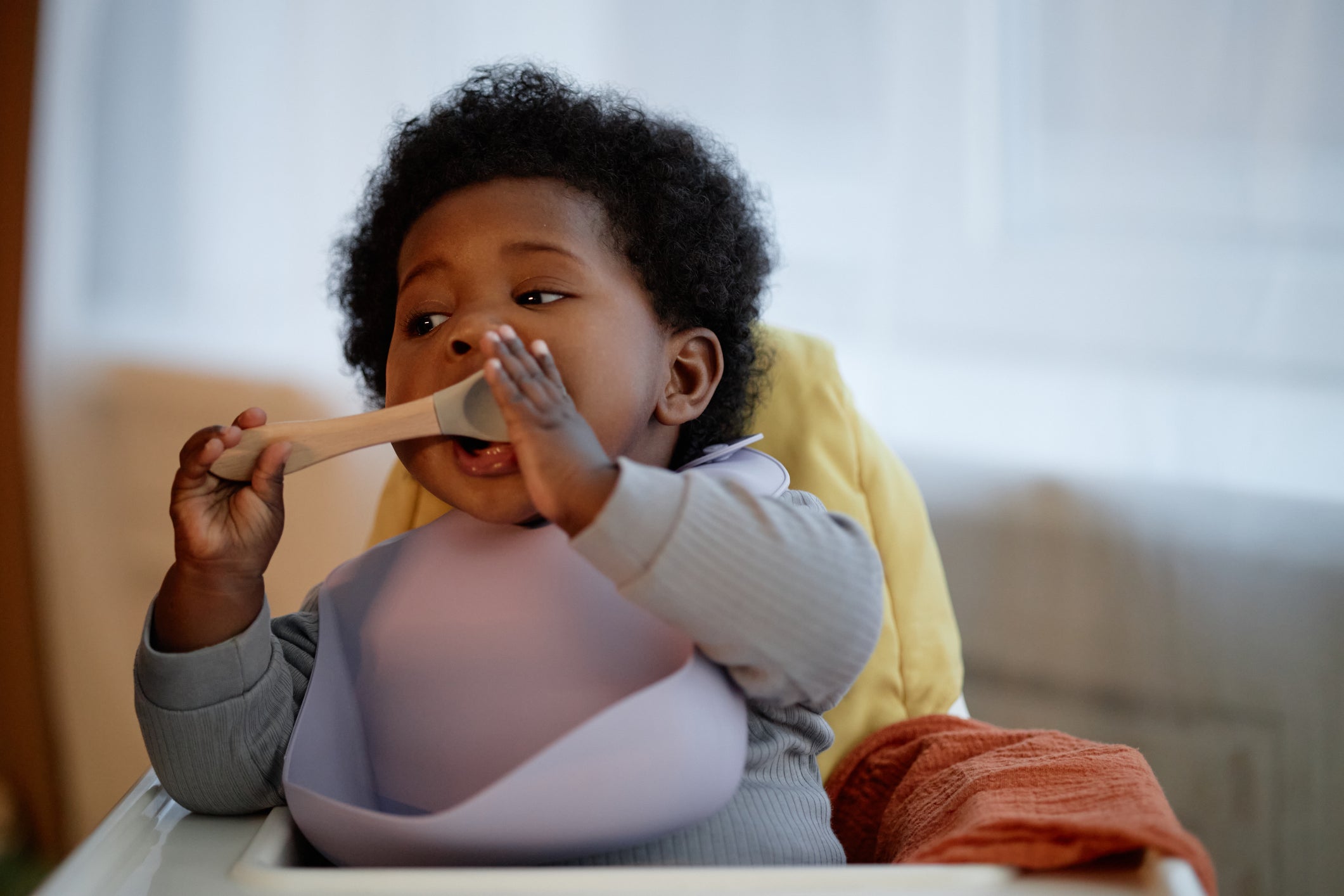 Child eating with a spoon in a high chair